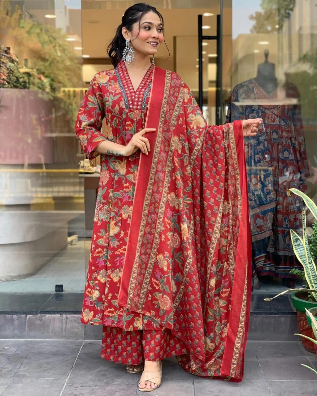 Woman in a red floral traditional outfit standing in front of a store window.