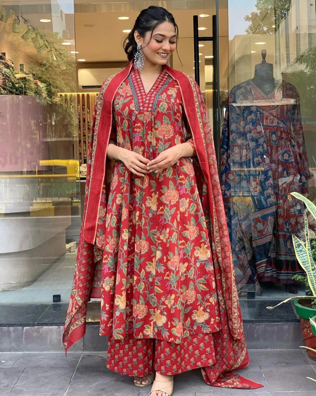 Woman in a red floral traditional outfit standing in front of a store entrance.