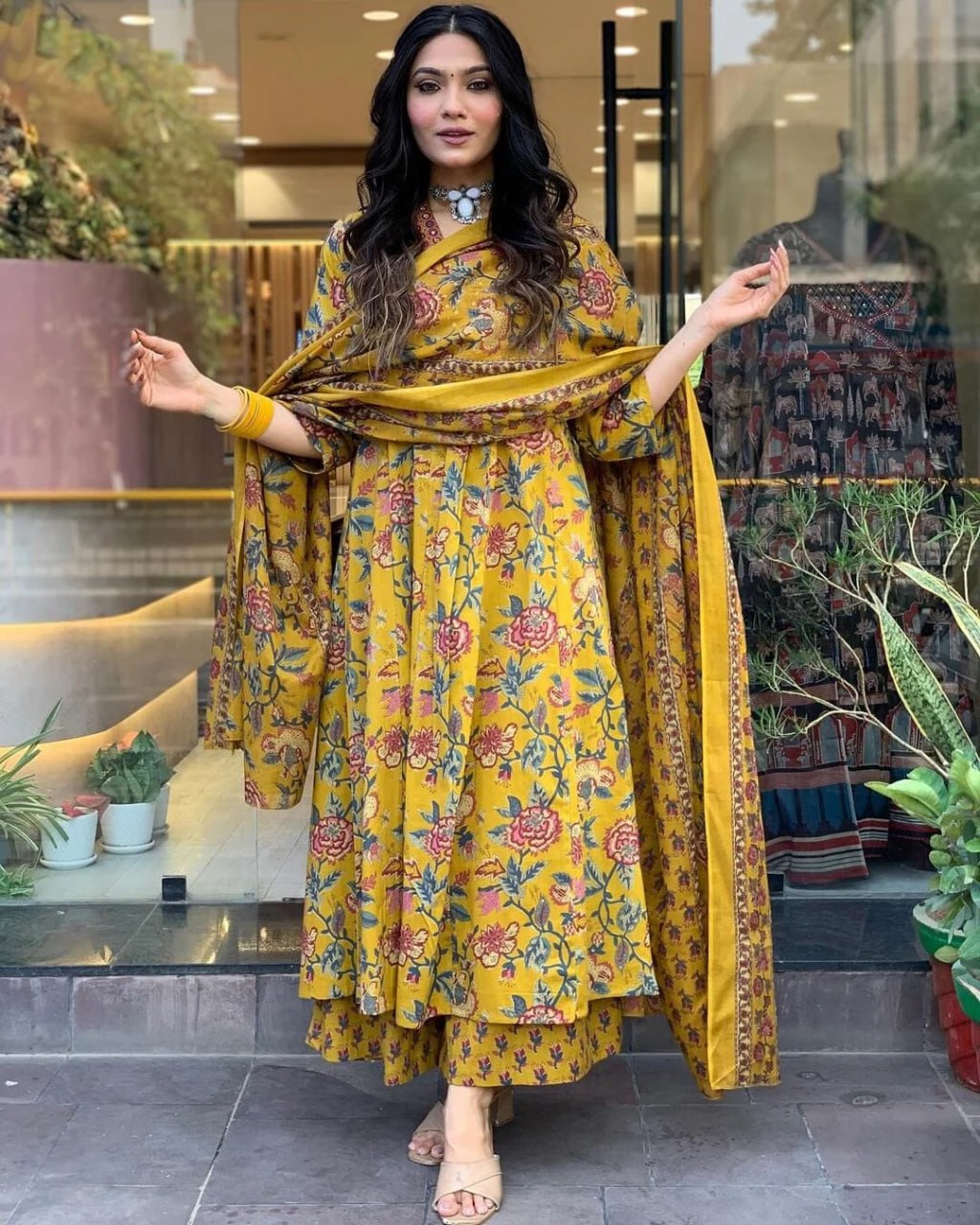 Woman in a yellow floral dress standing in front of a store entrance.