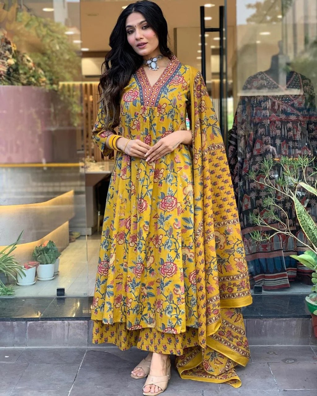 Woman wearing a yellow floral dress in an indoor setting with plants and decor.